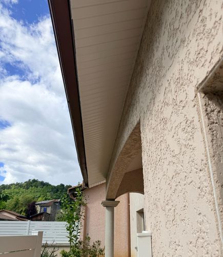 Sous-face en lambris PVC crème refermant le débord de toit, le long d’une gouttière brune